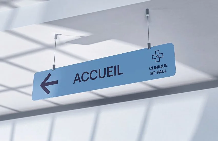 Un panneau suspendu « Accueil » avec sa flèche, dans un couloir de clinique
